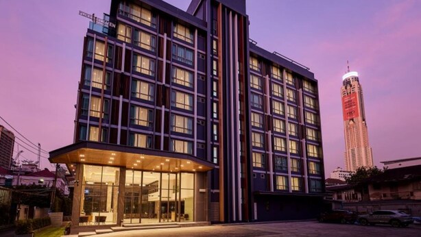 Un hotel moderno con fachada de vidrio, varios pisos y un edificio destacado al fondo.