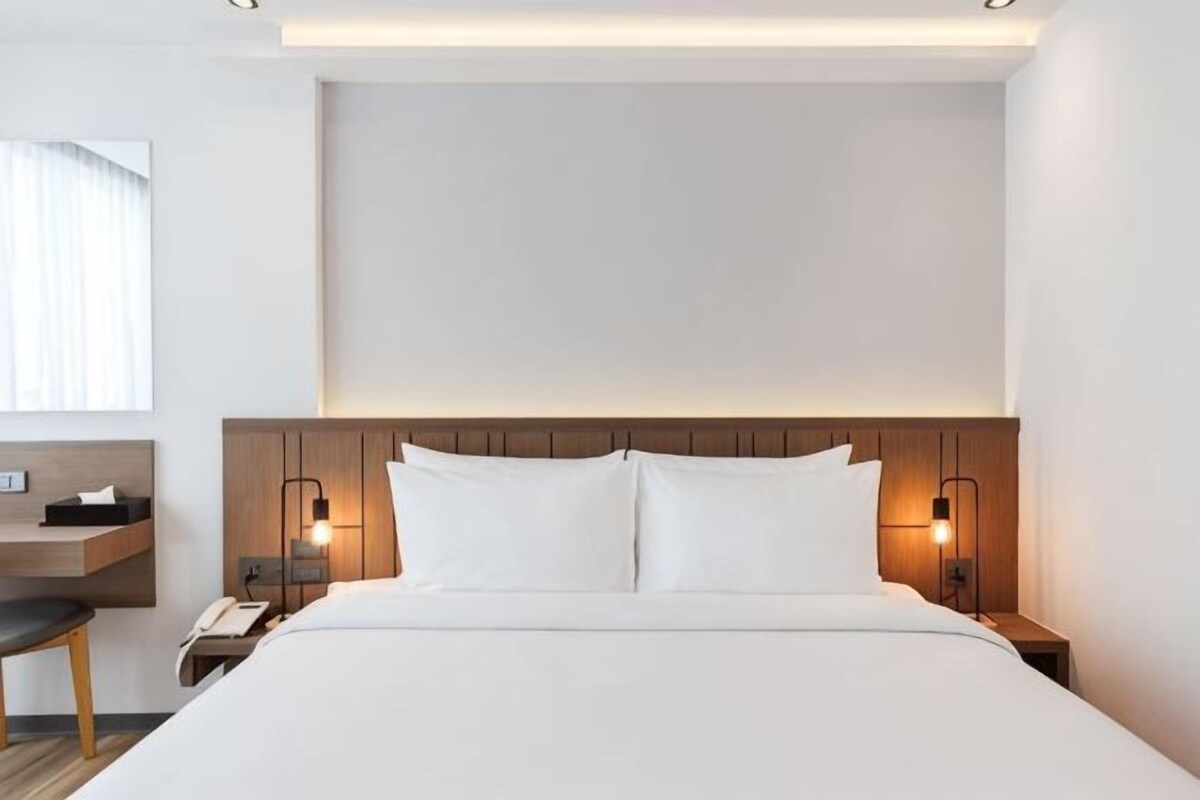 Une chambre d’hôtel avec un grand lit, une tête de lit en bois, des lampes de chevet, un bureau et une chaise.