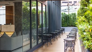 Un área de estar al aire libre moderna con paredes de vidrio, suelo de madera y sillas de metal negro.