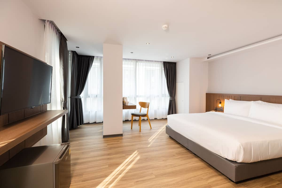 A modern hotel room with a large bed, a flat-screen TV, wooden flooring, and a desk with a chair.