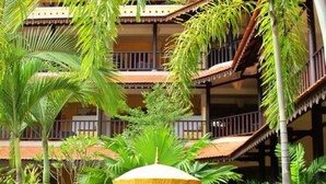 A courtyard with a statue of a seated figure under a canopy, surrounded by lush greenery and a multi-level building with balconies. - Le Siddharta D'Angkor (Siem Reap)