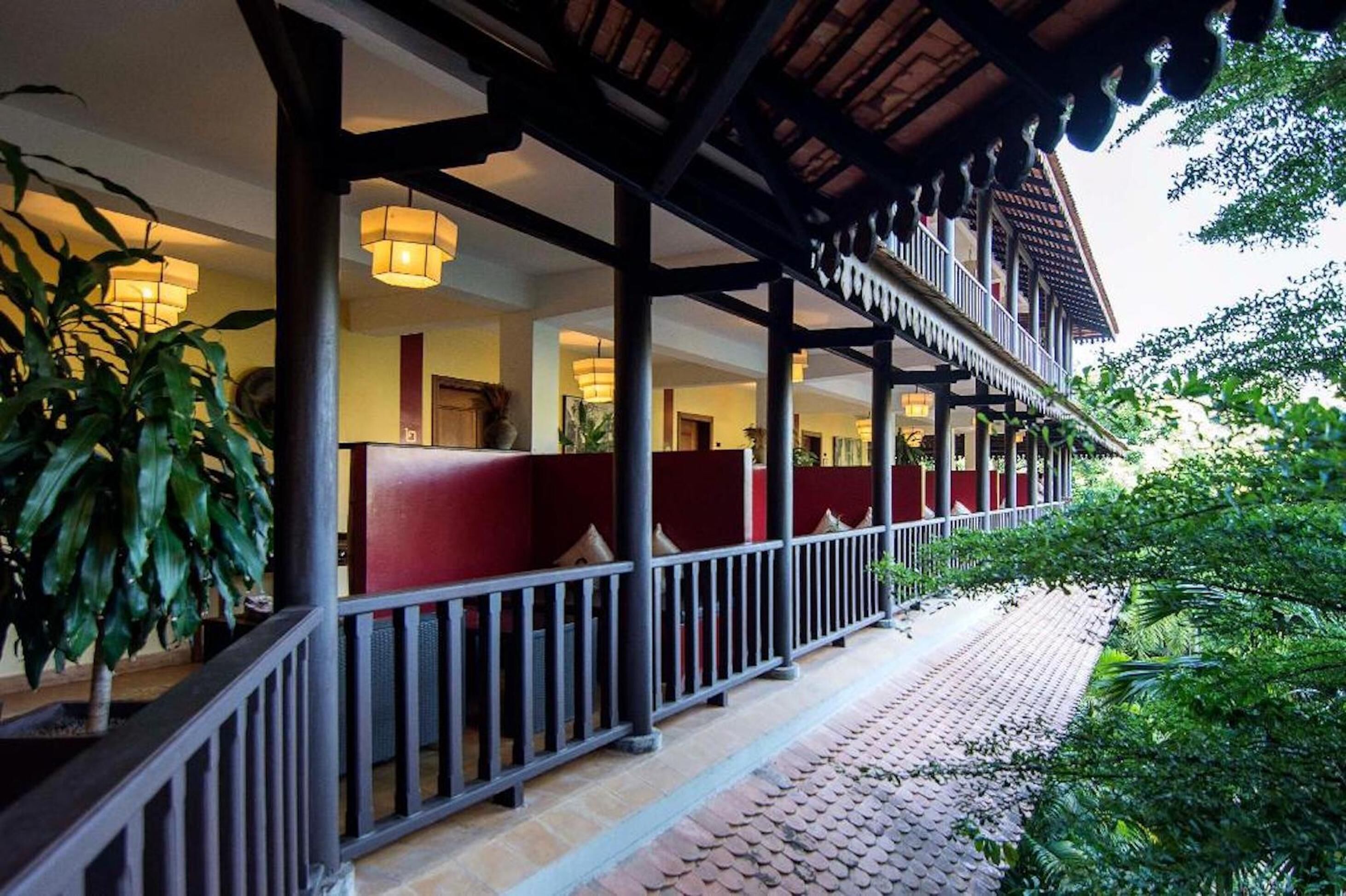A covered outdoor area with red seating, a tiled walkway, and greenery.