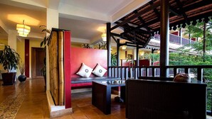 A lobby with a red wall, a wooden bench with cushions, a black wicker sofa, and a tiled floor. - Le Siddharta D'Angkor (Siem Reap)