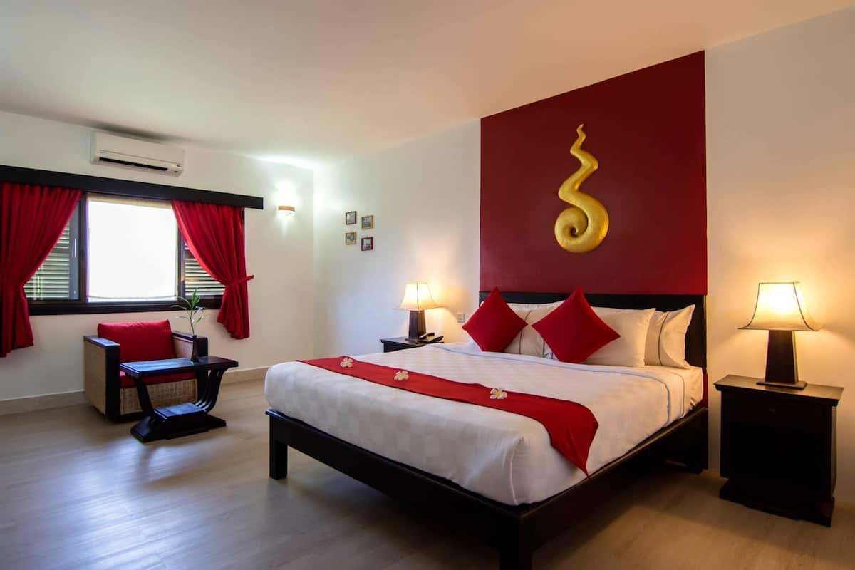 Habitación de hotel con cama, escritorio, silla y ventana con cortinas rojas.