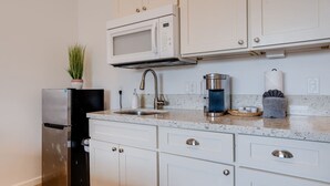 Una cocina con armarios blancos, un refrigerador de acero inoxidable, un microondas, una cafetera y un fregadero.