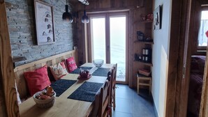 A rustic wooden interior with a dining table, chairs, and a bench. There are hanging lights, a framed picture on the wall, and a view through a glass door. - Direct access to the slopes & village center; parking included. South-facing terrace. Cozy & comfortable 3* (Courchevel)
