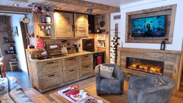 A cozy living room with a fireplace, wooden furniture, and a television mounted above it. - Direct access to the slopes & village center; parking included. South-facing terrace. Cozy & comfortable 3* (Courchevel)