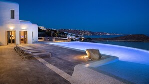 A modern building with a pool area, outdoor seating, and a view of the sea. - Villa Aliki  Panoramic view  Mykonos (Mykonos)