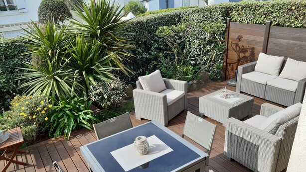 Une terrasse extérieure aménagée avec des meubles en osier, une table et diverses plantes.