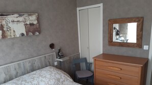 Une chambre à coucher comprenant un lit, une commode en bois, une chaise, un miroir fixé au mur et un objet décoratif portant le mot « Paix ».