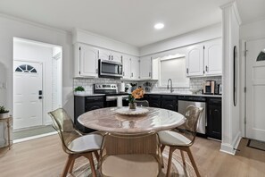 A modern kitchen with white cabinetry, a central island with chairs, and a stainless steel refrigerator.