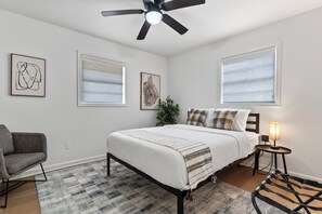 A bedroom with a bed, a chair, a bedside table with a lamp, and artwork on the walls.