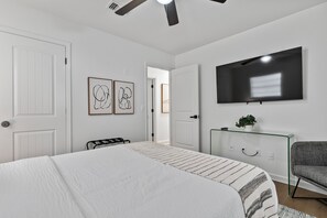 A bedroom with a bed, a TV mounted on the wall, a door, and a window.