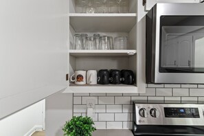 A kitchen with white cabinets, a microwave, a coffee maker, and a potted plant.