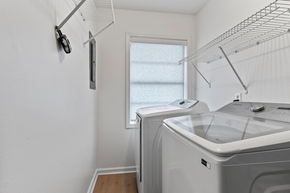 A laundry room with a washing machine and dryer, a window, and a drying rack.