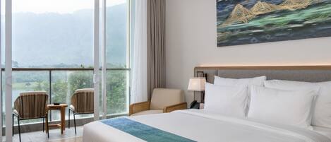 Une chambre d’hôtel avec un grand lit, une vue sur les montagnes par la fenêtre, un tableau au mur et deux fauteuils près de la fenêtre.