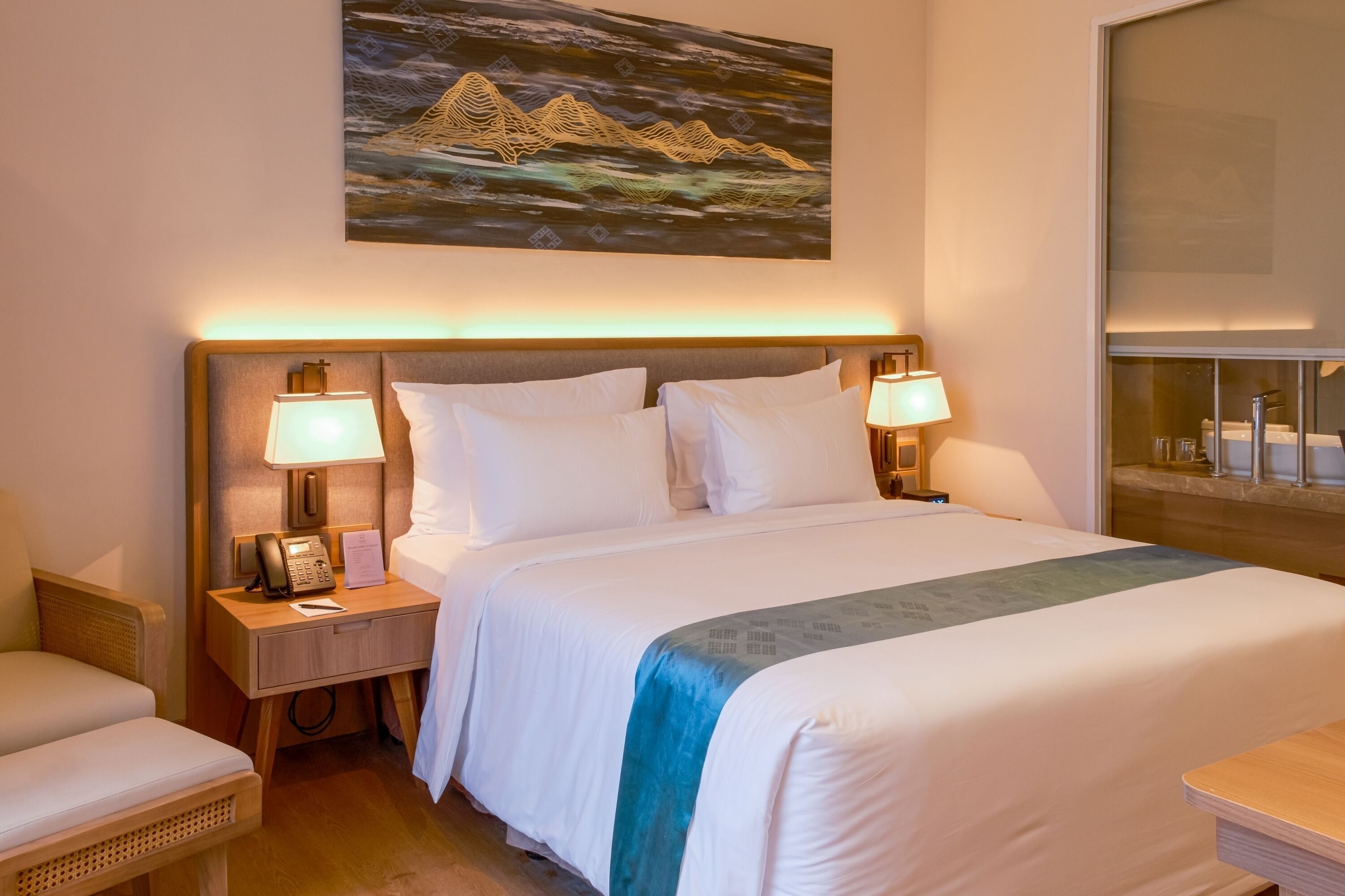 Ein Hotelzimmer mit einem großen Bett, zwei Nachttischen mit Lampen, einem Holzkopfende und einem Gemälde über dem Bett.
