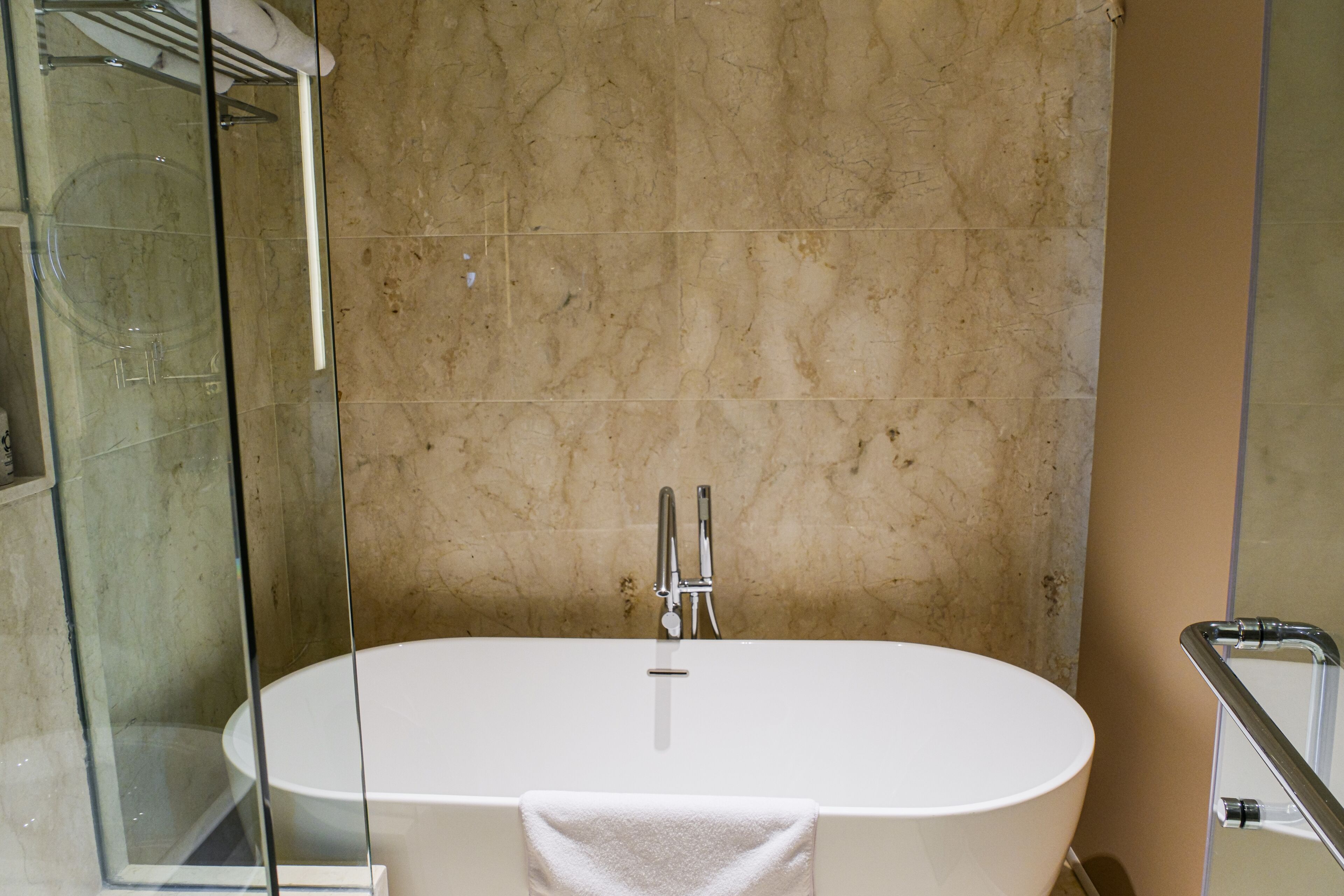 Un baño con bañera independiente, cabina de ducha de vidrio y pared de mármol.
