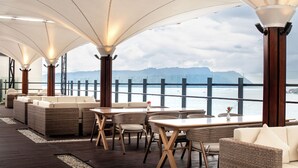 Una terrazza esterna con mobili in vimini, pavimento in legno e vista sul mare e sulle montagne.
