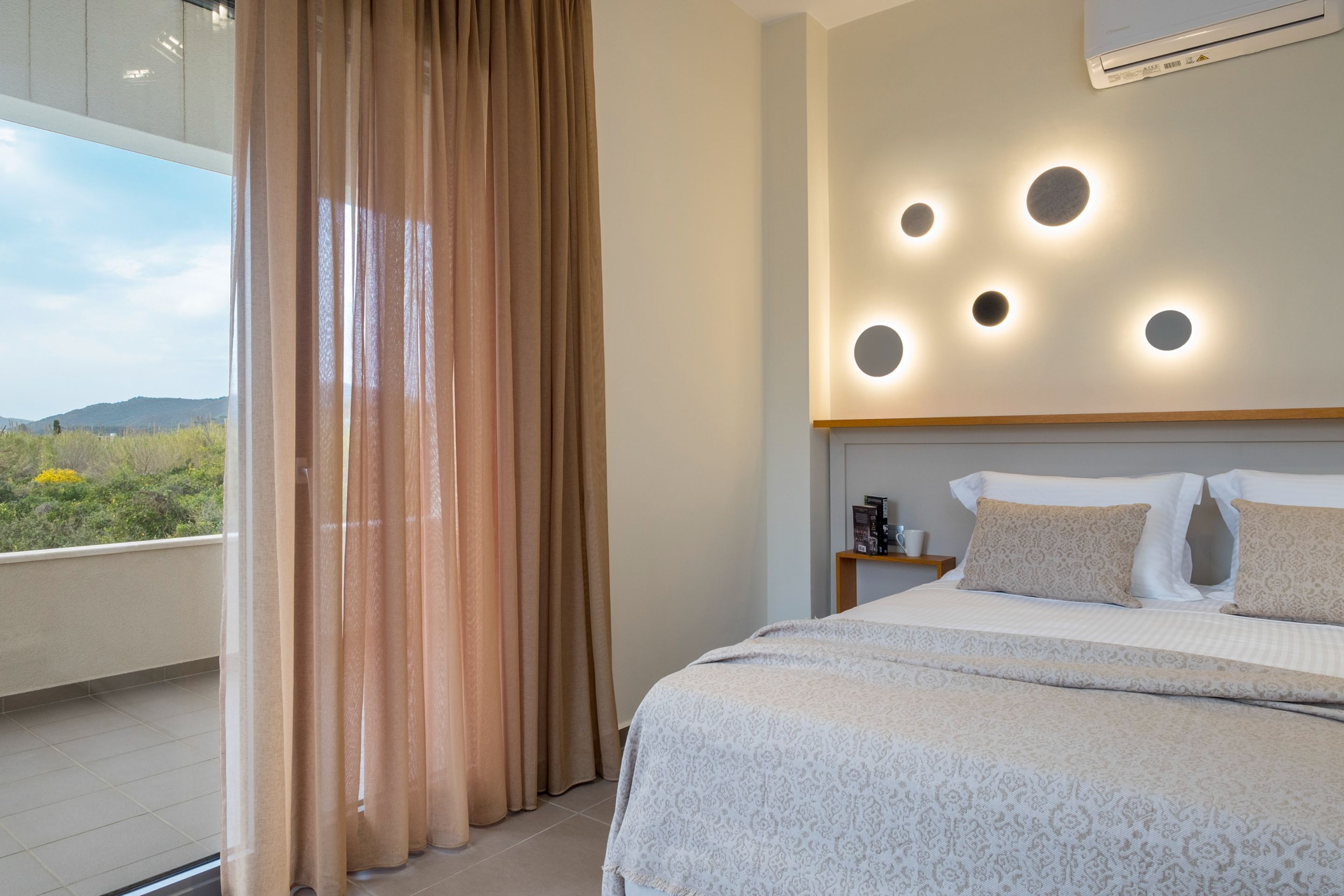Un dormitorio con una cama grande, una mesita de noche, una lámpara de techo y vistas al exterior.