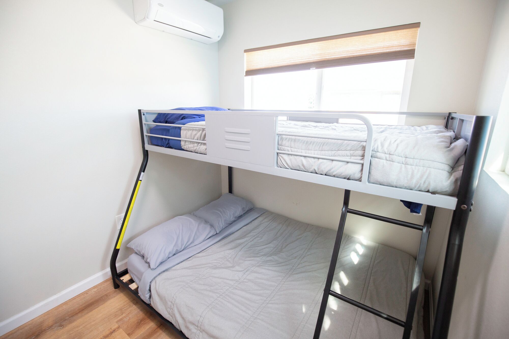 Dormitorio con literas, ventana, aire acondicionado blanco y piso de madera.
