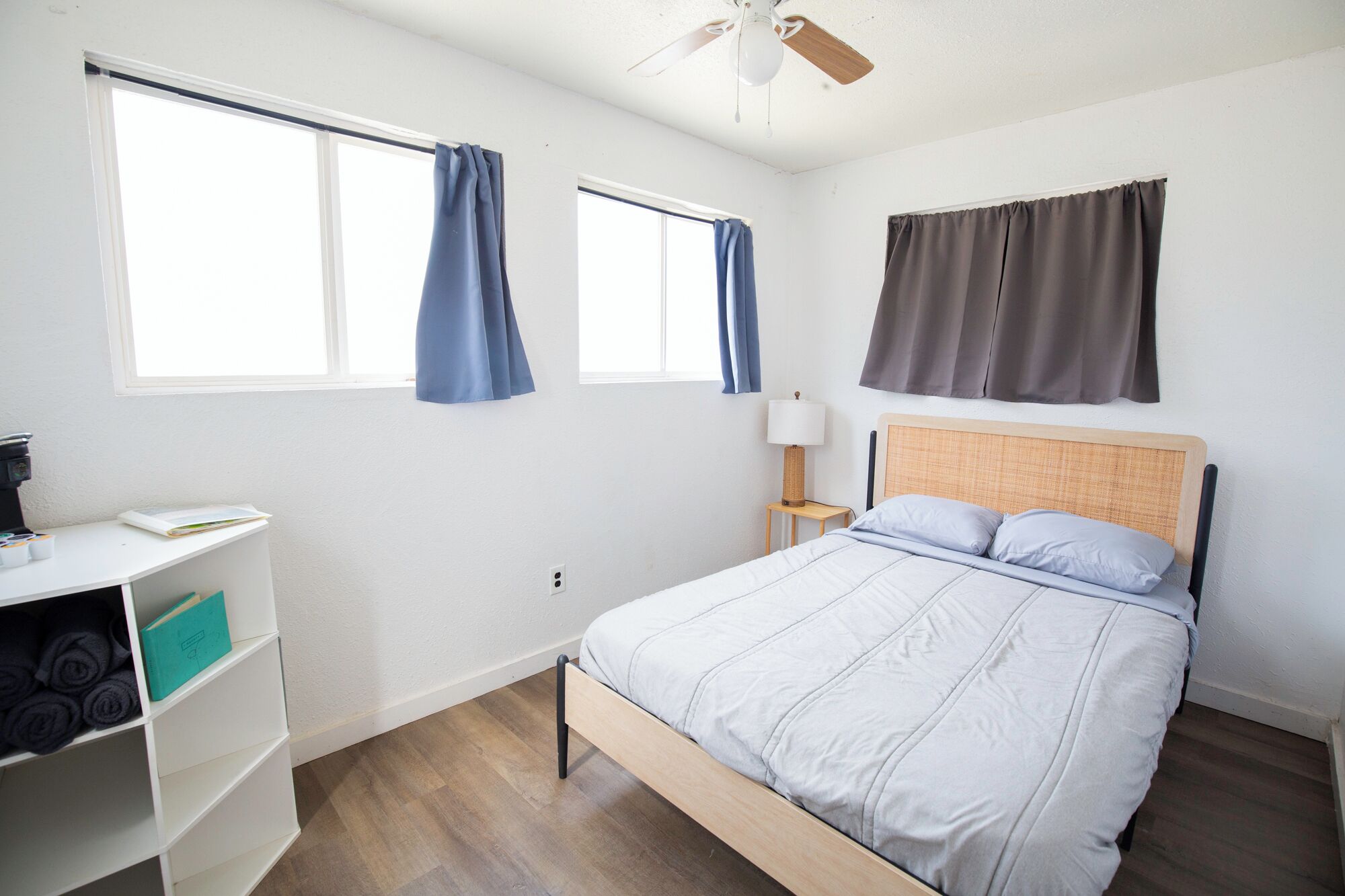 Une chambre à coucher avec un lit, un bureau avec une lampe et deux fenêtres avec des rideaux.