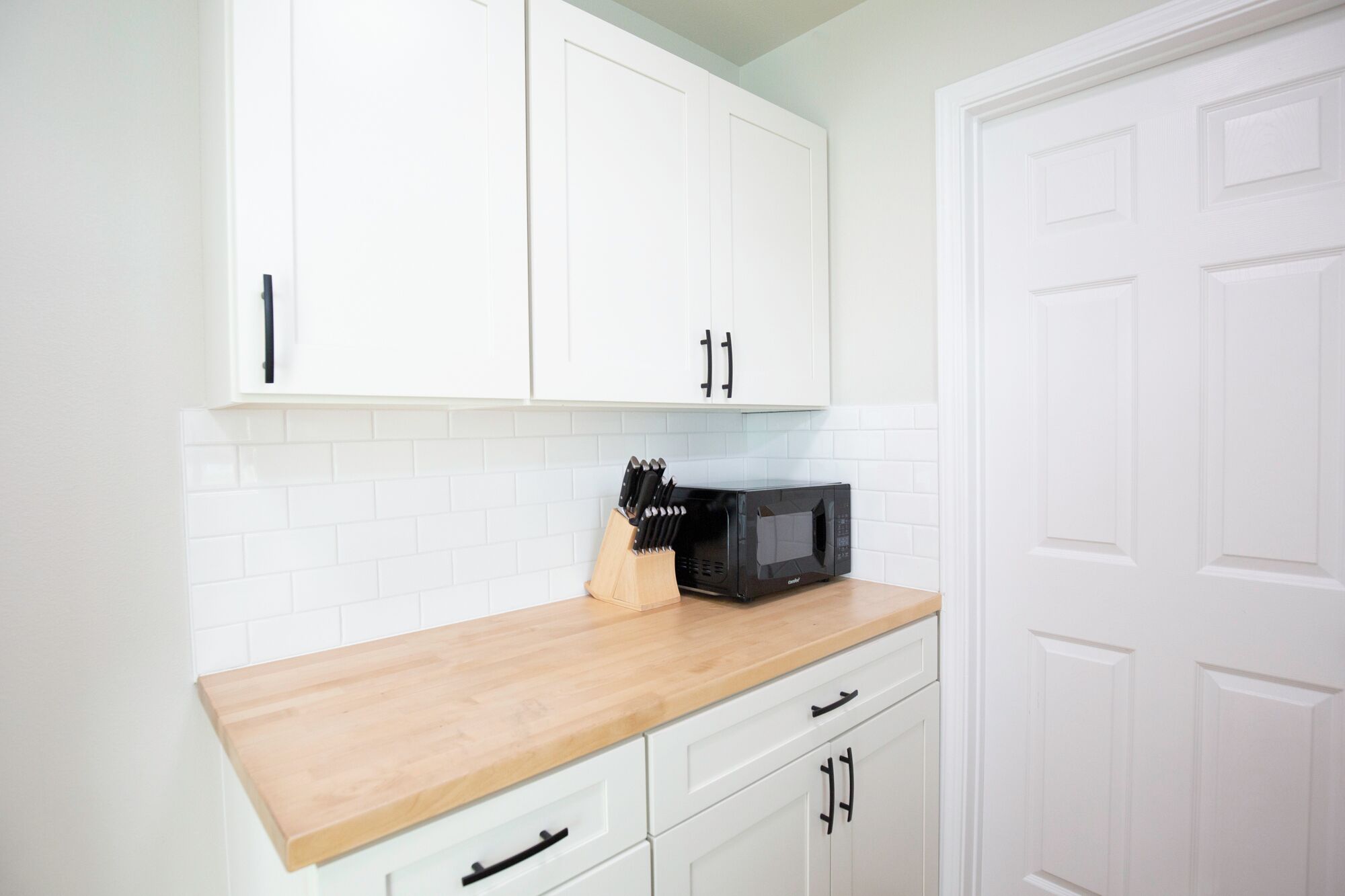 A kitchen with white cabinets, a wooden countertop, and a black microwave.