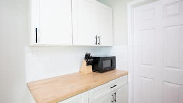 Cozinha com armários brancos, bancada de madeira e micro-ondas preto.
