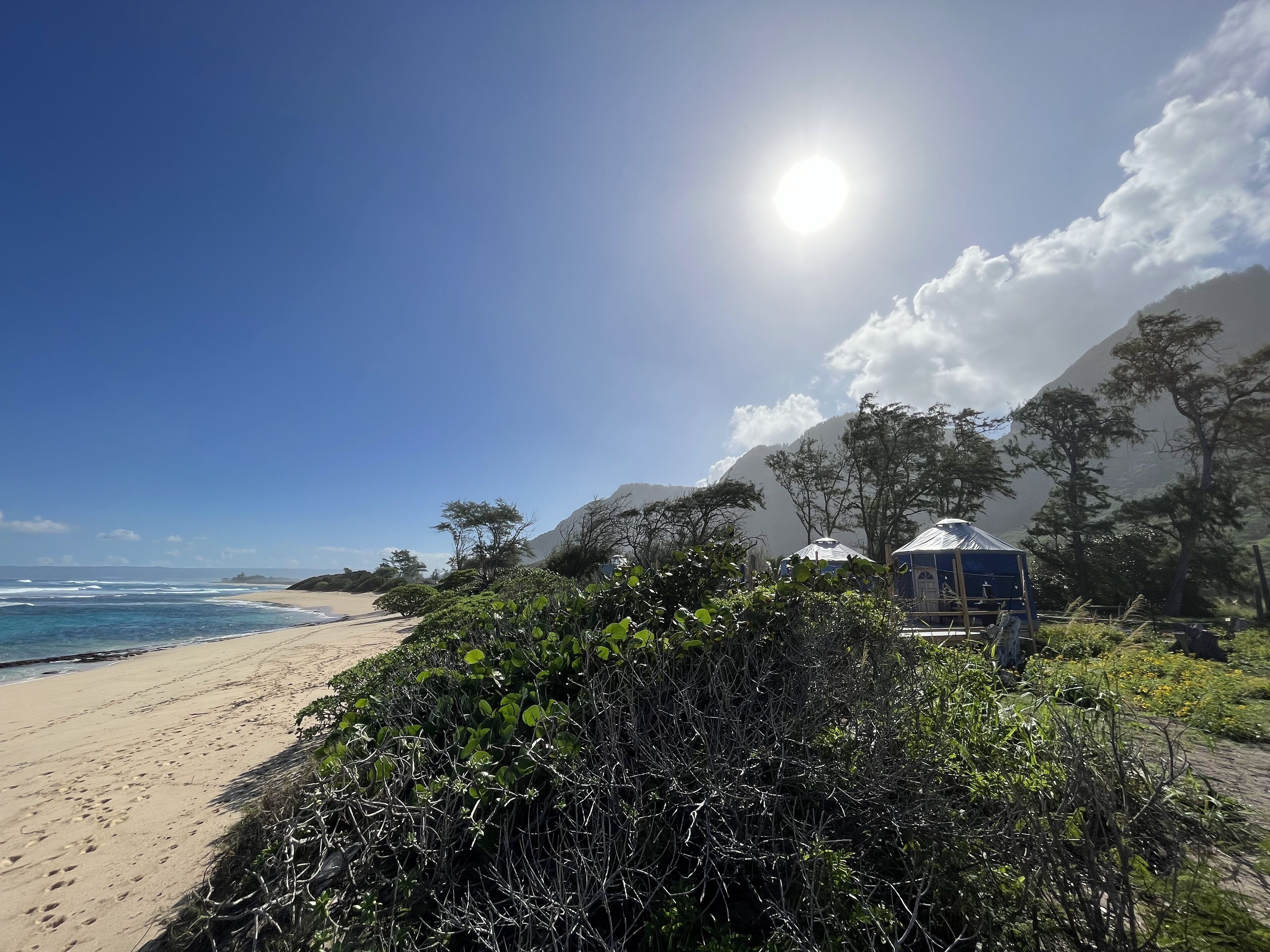 A beach with a clear sky, ocean waves, and a small structure with a blue roof.