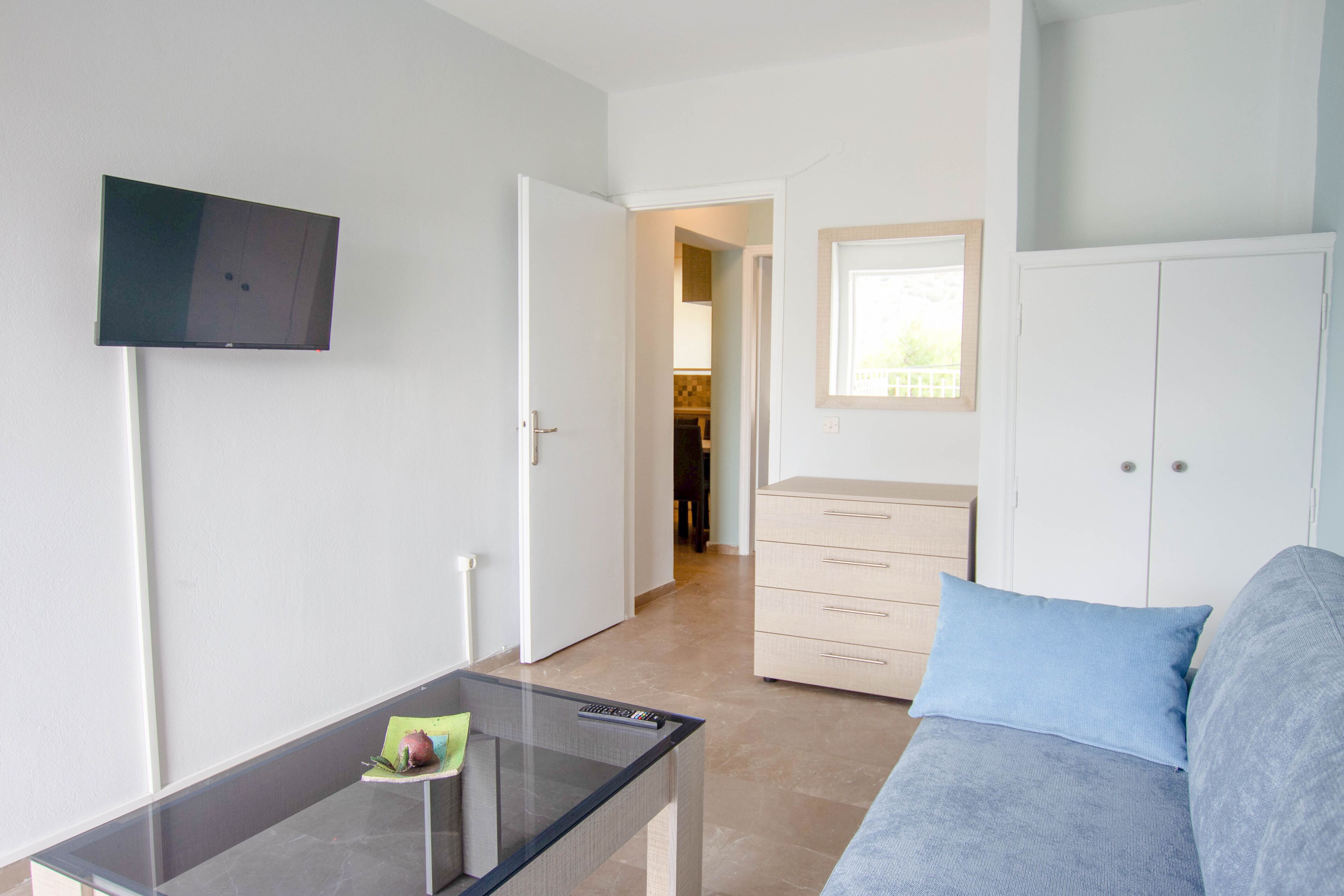 A bedroom with a bed, a TV mounted on the wall, a desk with a remote control, and a wardrobe.