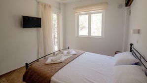 A bedroom with a bed, a flat-screen TV mounted on the wall, a window with curtains, and a ceiling light. - Akrotopi Apartments (Nafplio)