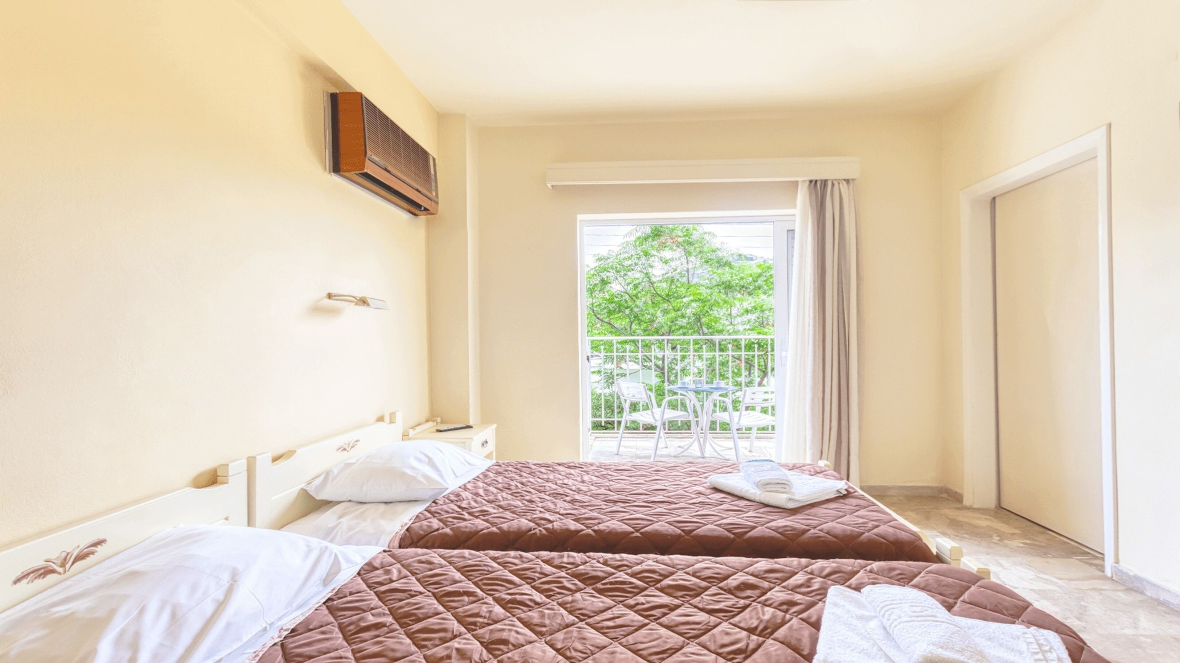 Habitación de hotel con dos camas, un balcón y vista a árboles, y un ventilador de techo.