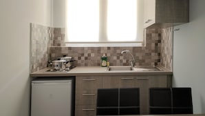 A compact kitchen with a window, a sink, a stove, and a refrigerator. - Akrotopi Apartments (Nafplio)