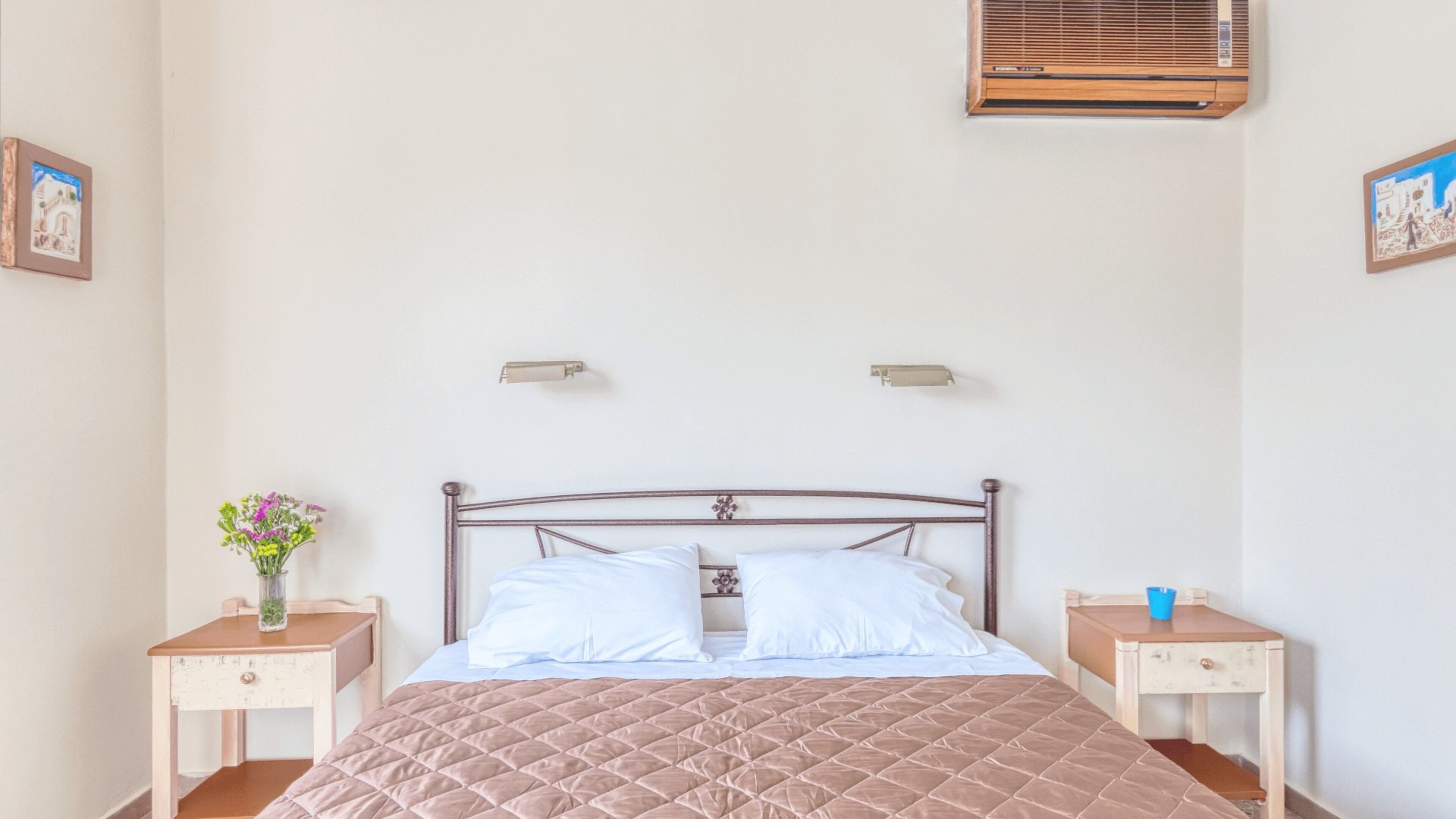 Une chambre à coucher comprenant un lit, deux tables de chevet, une commode, un climatiseur fixé au mur et deux lampes murales.