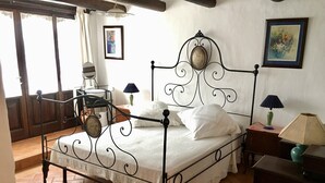 Un dormitorio con estructura de cama metálica, ropa de cama blanca, una lámpara verde y un cuadro en la pared.