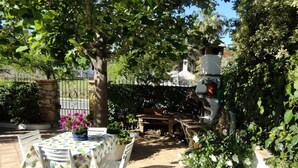 Un patio al aire libre con una mesa redonda y sillas, rodeado de vegetación exuberante y plantas en macetas.