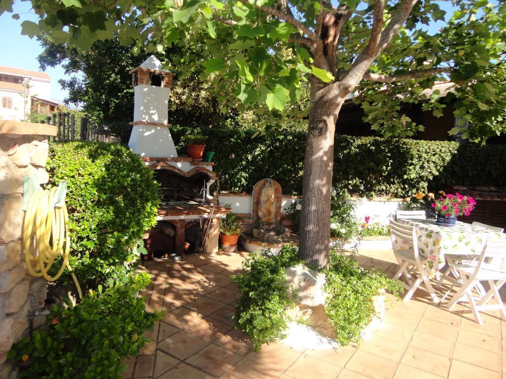 Un patio con pared de piedra, chimenea blanca, plantas en macetas y una mesa con sillas.