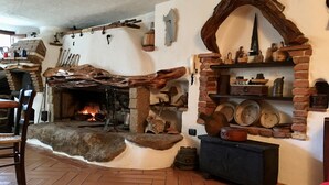 Un interior rústico con chimenea de piedra, vigas de madera y una estantería de ladrillo con cerámica.