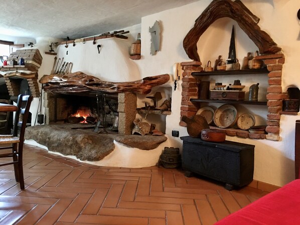Un interior rústico con chimenea de piedra, vigas de madera y una estantería de ladrillo con cerámica.