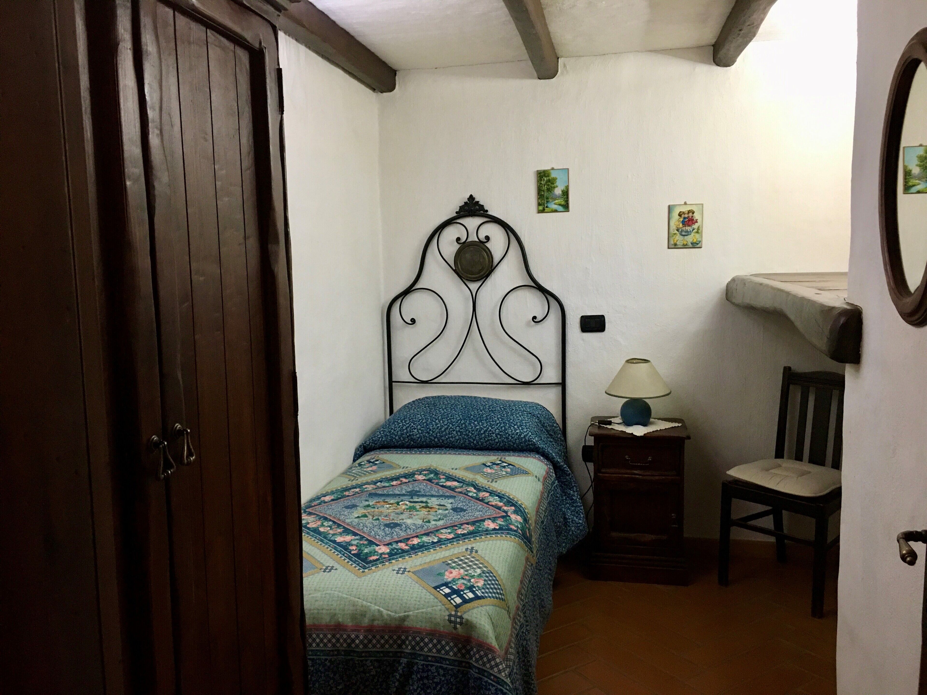 A bedroom with a bed, a chair, a nightstand with a lamp, and a wooden wardrobe.
