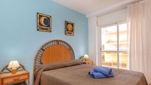 Un dormitorio con cabecera de madera, una cama con colcha marrón, una mesita de noche con lámpara y dos signos del zodiaco colgados en la pared.