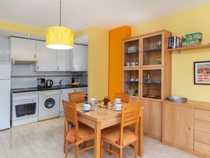 Een kleine keuken met een eettafel, stoelen, een wasmachine, een fornuis en een kast met glazen deuren.