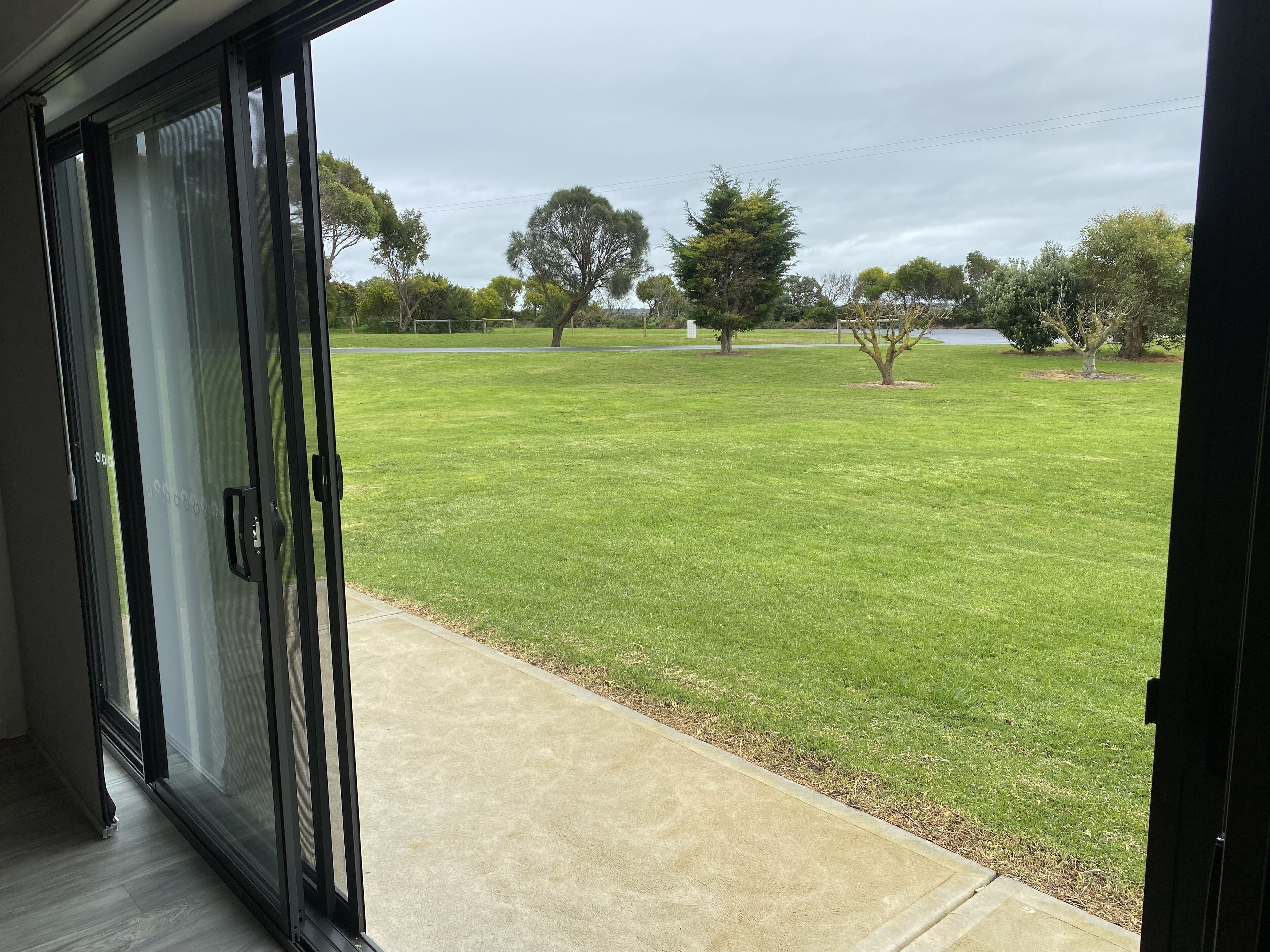 A view from inside a building looking out to a well-maintained lawn with trees and a body of water in the distance.