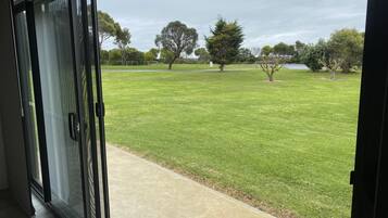 A view from inside a building looking out to a well-maintained lawn with trees and a body of water in the distance.