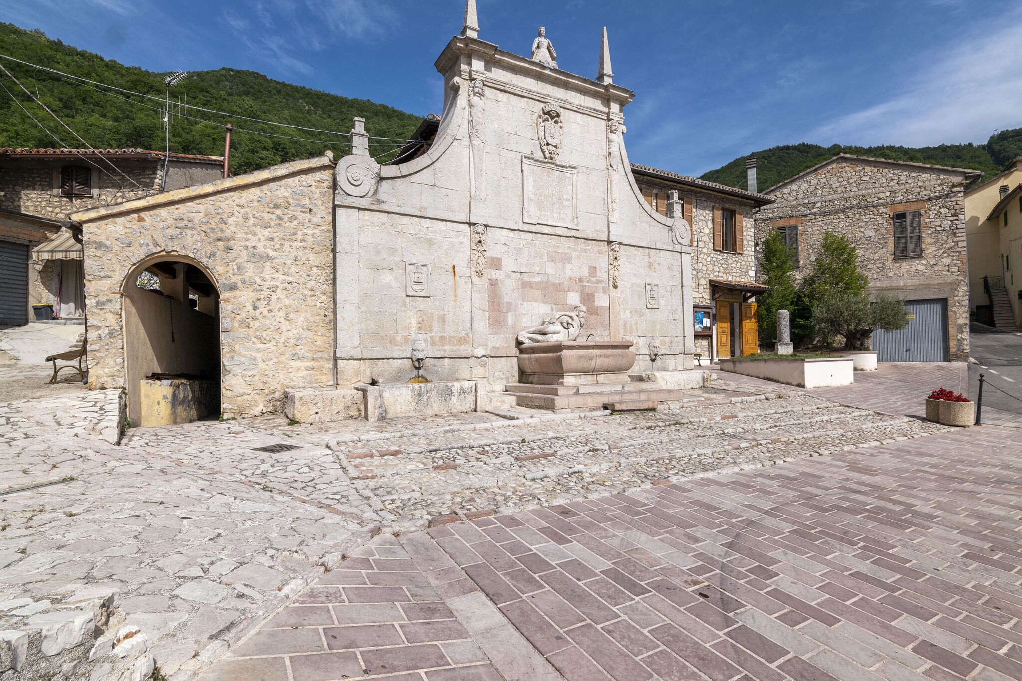 Un edificio de piedra con una torre de reloj, una estatua y un patio empedrado.