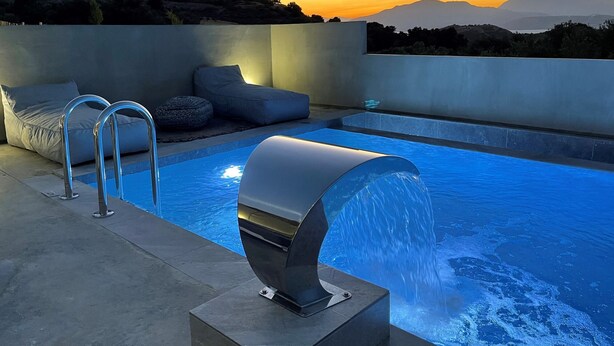 Piscina moderna ao ar livre com um elemento aquático, áreas de estar e vista para as montanhas.