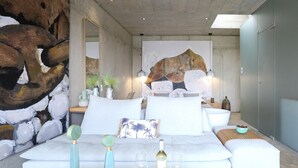 Uma sala de estar moderna com um sofá branco, uma mesa de centro de madeira e um grande quadro abstrato na parede.