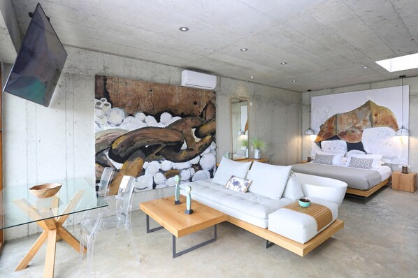 A modern living room with a glass coffee table, white sofa, and a large abstract painting on the wall.
