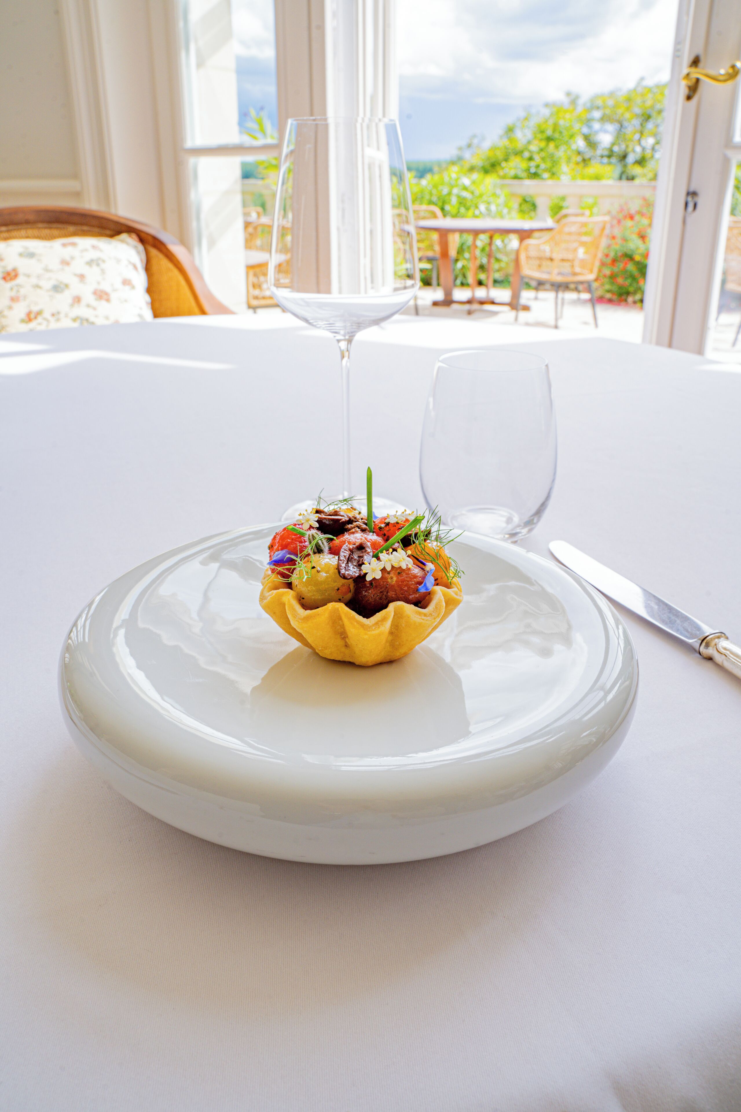 Una mesa de comedor con mantel blanco, un cuenco de vidrio con base amarilla y una copa de vino.