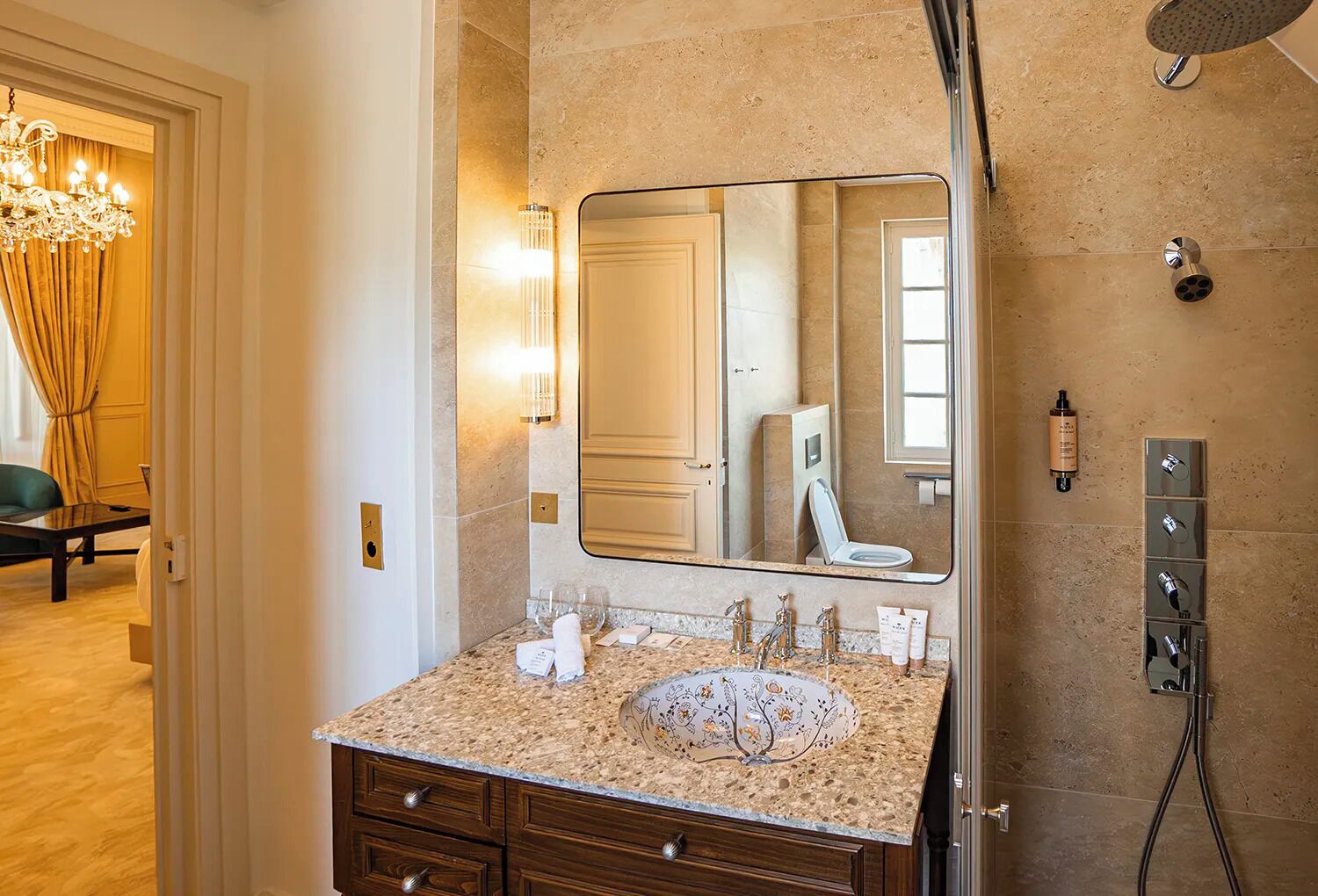 A bathroom with a large mirror, a sink with multiple faucets, a showerhead, and a towel rack.